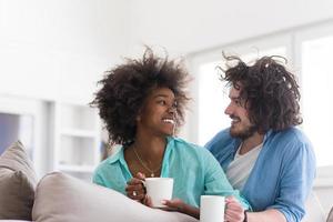 casal multiétnico sentado no sofá em casa bebendo café foto