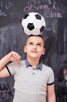 menino feliz segurando uma bola de futebol na cabeça foto