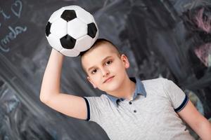 menino feliz segurando uma bola de futebol na cabeça foto