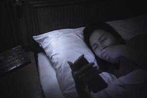 mulher asiática jogando no smartphone na cama à noite, tailândia, viciado em mídia social foto