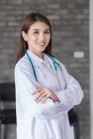 médica profissional mulher asiática em pé com os braços cruzados feliz e sorriso no hospital. vestindo uma túnica branca e estetoscópio foto