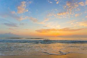 uma foto do mar está lambendo a praia de areia no pôr do sol da noite. céu azul laranja com fundo de vista para o mar.