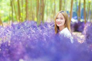 mulher asiática sorri alegremente no jardim de flores roxas como primeiro plano no tema natural. foto