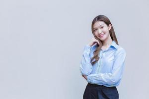 jovem mulher trabalhadora de negócios asiáticos com cabelos longos que vestem uma camisa azul de manga comprida sorri alegremente enquanto ela cruza os braços para apresentar algo sobre fundo branco. foto