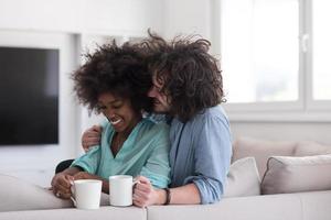 casal multiétnico sentado no sofá em casa bebendo café foto