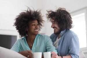 casal multiétnico sentado no sofá em casa bebendo café foto