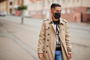 homem elegante kuwaitiano no trench coat usa máscara facial preta durante a pandemia covid. foto