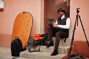 jovem cinegrafista americano africano profissional segurando câmera profissional com equipamento profissional. cinegrafista afro vestindo duraq preto fazendo vídeos. foto