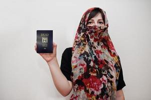 jovem muçulmana árabe em roupas hijab detém o passaporte do estado de israel no fundo da parede branca, retrato de estúdio. foto