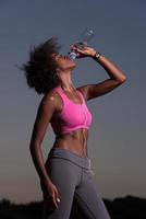 mulher afro-americana bebendo água depois de correr na natureza foto