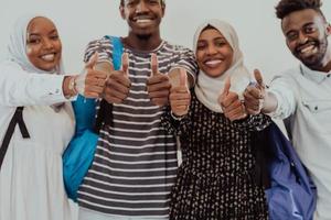 retrato de grupo de estudantes africanos felizes juntos contra um fundo branco e mostrando sinal de ok polegares para cima meninas vestindo a moda tradicional do hijab muçulmano do sudão foto