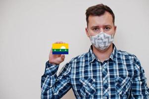 homem de camisa quadriculada mostra cartão de bandeira nueva esparta na mão, use máscara de proteção isolada no fundo branco. conceito de coronavírus de países americanos. foto