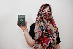 jovem mulher muçulmana árabe em roupas de hijab detém o passaporte da república democrática da argélia popular no fundo da parede branca, retrato de estúdio. foto