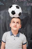 menino feliz segurando uma bola de futebol na cabeça foto