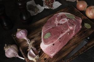 bife de porco cru em uma velha tábua, faca, especiarias e ingredientes são dispostos lado a lado.