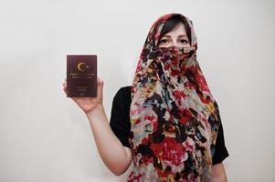 jovem muçulmana árabe em roupas hijab segura passaporte da república da turquia no fundo da parede branca, retrato de estúdio. foto
