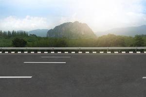 visão horizontal do vazio turva da estrada de asfalto com beira da estrada. fundo de floresta verde e montanhas sob o céu azul com nuvens brancas. foto