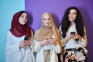 mulheres muçulmanas usando telefones celulares isolados em fundo azul e roxo foto