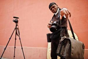 jovem cinegrafista americano africano profissional segurando câmera profissional com equipamento profissional. cinegrafista afro vestindo duraq preto fazendo vídeos. foto