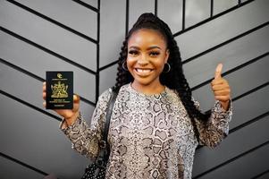 feche o retrato de uma jovem afro-americana positiva segurando o passaporte de trinidad e tobago e polegares para cima. foto