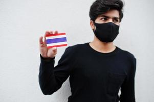 homem asiático usar todo preto com máscara facial segurar a bandeira da tailândia na mão isolada no fundo branco. conceito de país coronavírus. foto