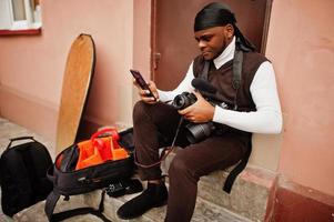 jovem cinegrafista americano africano profissional segurando câmera profissional com equipamento profissional. cinegrafista afro vestindo duraq preto fazendo vídeos. foto