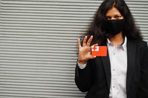 mulher asiática com roupa formal e máscara protetora preta segura a bandeira de tonga à mão contra um fundo cinza. coronavírus no conceito de país. foto