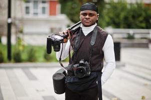 jovem cinegrafista americano africano profissional segurando câmera profissional com equipamento profissional. cinegrafista afro vestindo duraq preto fazendo vídeos. foto