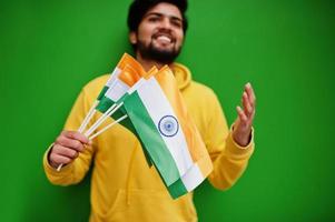 homem indiano urbano jovem hippie em um moletom amarelo na moda segura bandeiras da índia nas mãos. cara legal do sul da Ásia usa capuz isolado em fundo verde. foto