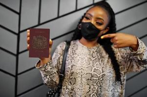 mulher africana usando máscara facial preta mostra passaporte de santa helena na mão. coronavírus no país africano, fechamento e quarentena de fronteiras, conceito de surto de vírus. foto