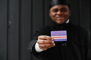 homem africano desgaste preto durag segure a bandeira de cabo verde à mão isolado fundo escuro. foto