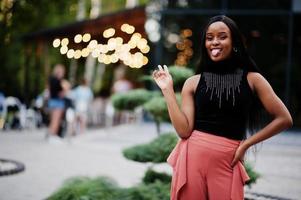 mulher afro-americana elegante em calças de pêssego e blusa preta posam ao ar livre.