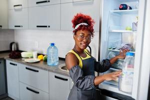 mulher afro-americana em casa cozinha aberta geladeira. foto