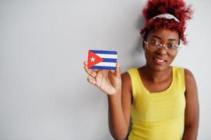 mulher afro-americana com cabelo afro, use camiseta amarela e óculos, segure a bandeira de cuba isolada no fundo branco. foto