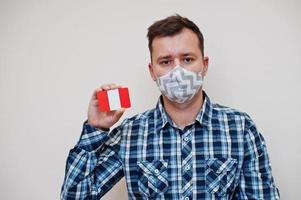 homem de camisa quadriculada mostra cartão de bandeira do peru na mão, use máscara de proteção isolada no fundo branco. conceito de coronavírus de países americanos. foto