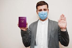 homem europeu com roupa formal e máscara facial, mostre o passaporte do kosovo com a mão do sinal de stop. bloqueio de coronavírus no conceito de país da europa. foto