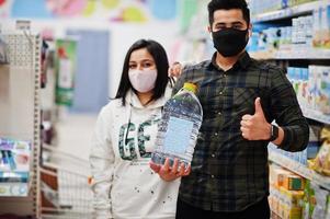 casal asiático usa máscara protetora fazendo compras juntos no supermercado durante a pandemia. homem segura garrafa com água. foto