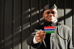 homem africano desgaste preto durag segure a bandeira da gâmbia à mão isolado fundo escuro. foto