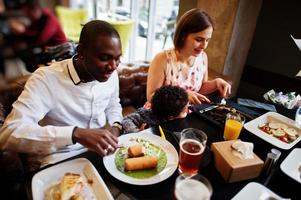 feliz família multiétnica com menino passa tempo no restaurante. relacionamentos de homem africano e mulher branca europeia. foto