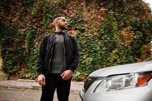 retrato de homem de barba árabe elegante usar gola alta cinza e jaqueta preta. cara modelo árabe fica perto de seu carro. foto