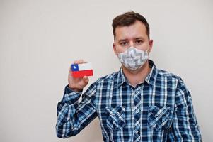 homem de camisa quadriculada mostra cartão de bandeira chile na mão, use máscara de proteção isolada no fundo branco. conceito de coronavírus de países americanos. foto