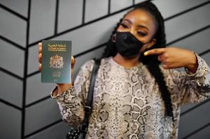 mulher africana usando máscara facial preta mostra passaporte marroquino na mão. coronavírus no país africano, fechamento e quarentena de fronteiras, conceito de surto de vírus. foto