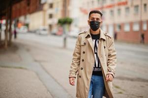 homem elegante kuwaitiano no trench coat usa máscara facial preta durante a pandemia covid. foto