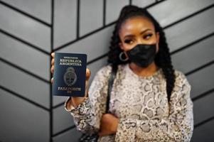 mulher afro-americana usando máscara facial preta mostra passaporte argentino na mão. coronavírus no país da américa, fechamento de fronteiras e quarentena, conceito de surto de vírus. foto