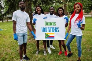 grupo de voluntários africanos felizes em branco com bandeira de comores no parque. países da África voluntariado, caridade, pessoas e conceito de ecologia. foto