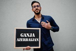 homem árabe usa camisa azul e óculos segura placa com inscrição de ganja azerbaijão. maiores cidades no conceito do mundo islâmico. foto