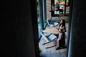 retrato da moda da mulher afro-americana em vestido longo, botas e óculos de sol indoor. foto