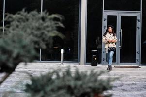 elegante mulher afro-americana usar boina e casaco com bolsa posando ao ar livre. foto