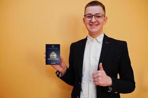 jovem bonito segurando a identificação do passaporte da república da guiana sobre fundo amarelo, feliz e aparecer o polegar. viajar para países da América. foto