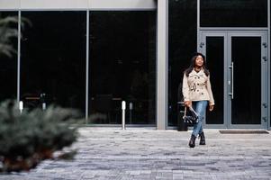 elegante mulher afro-americana usar boina e casaco com bolsa posando ao ar livre. foto